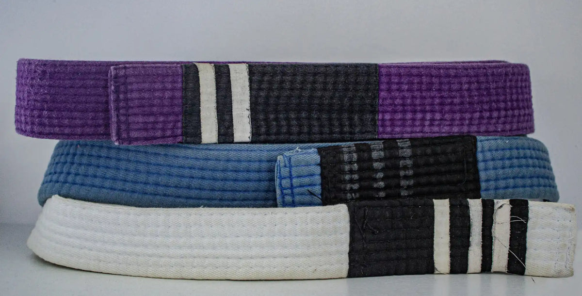 Three martial arts belts stacked together in purple, blue, and white with black striped sections.